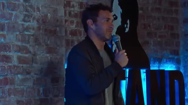 Mark Normand performing on a comedy club stage with a microphone.