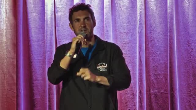 Mark Normand on stage in front of a purple curtain, working new material.